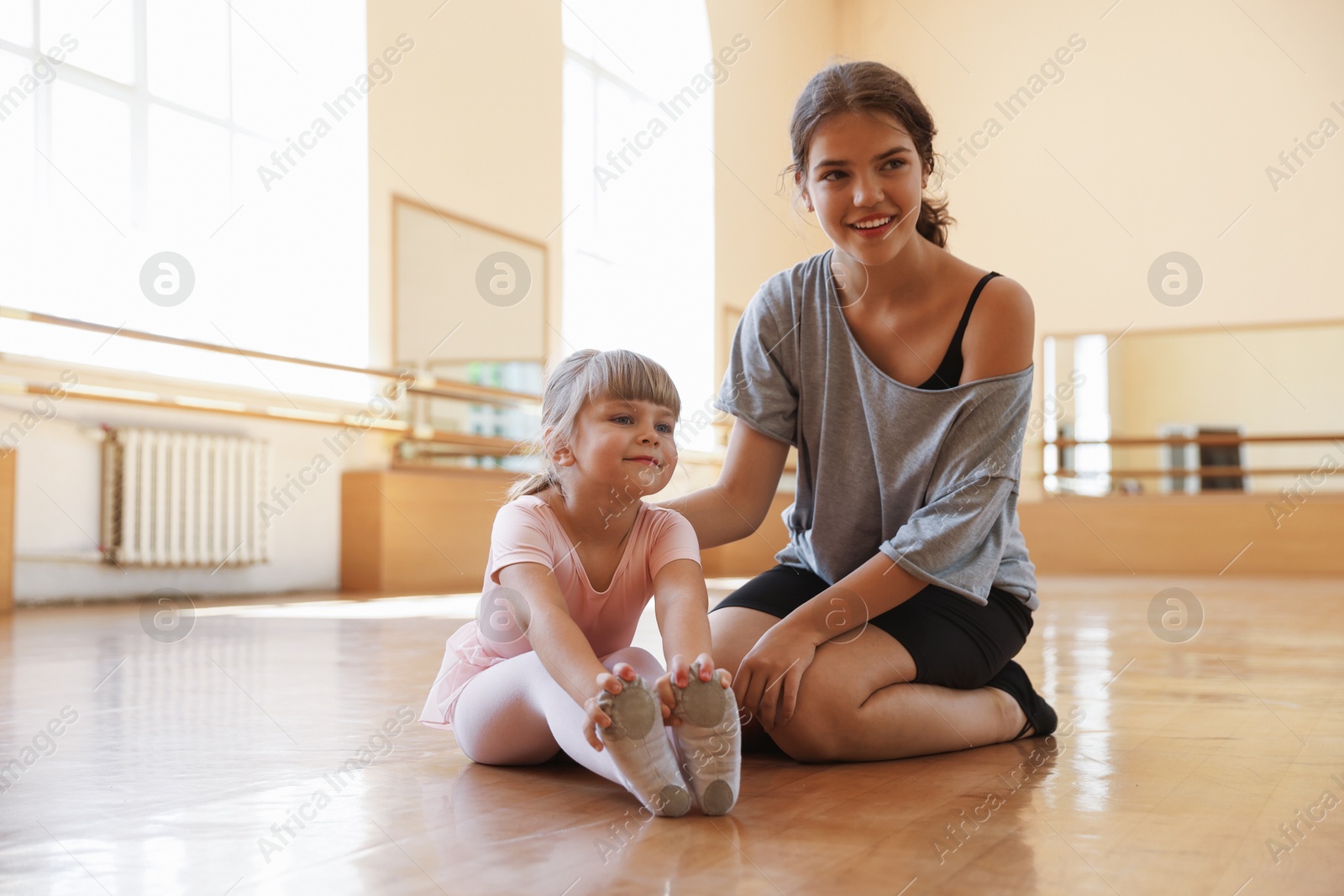 Happy ballet teacher working with little girl on floor in dance class Photo of Happy ballet teacher working with little girl on floor in dance class