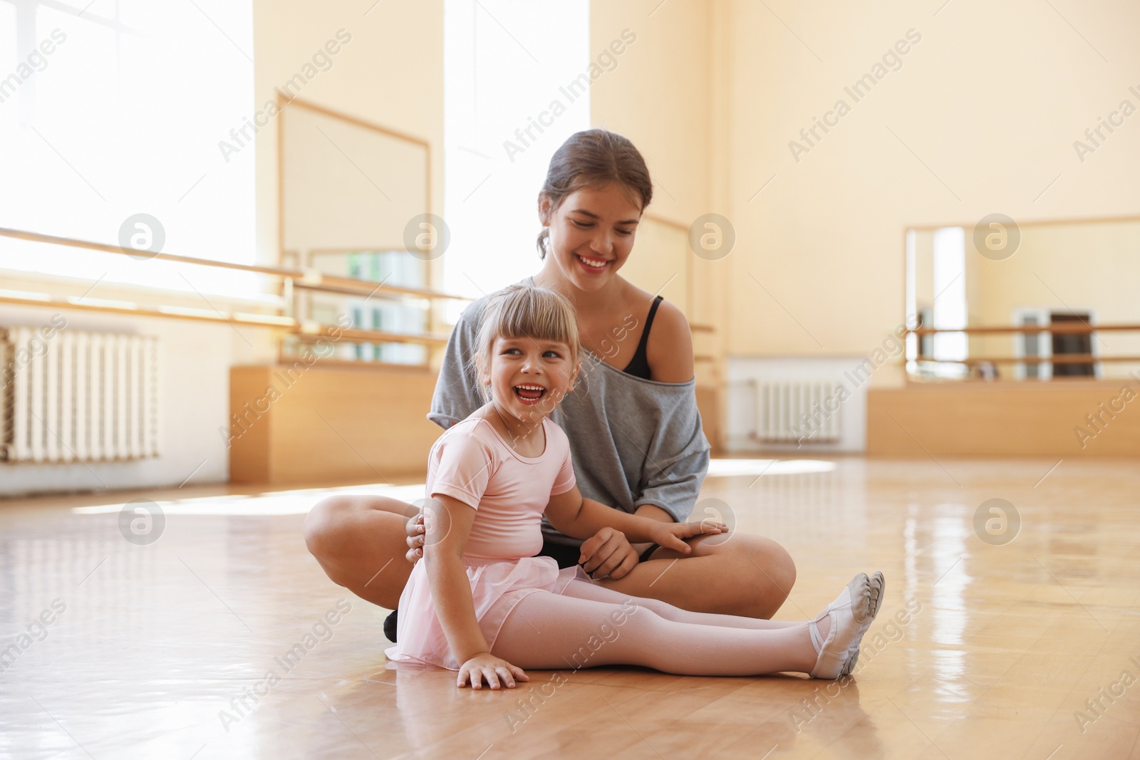 Happy ballet teacher working with little girl on floor in dance class Photo of Happy ballet teacher working with little girl on floor in dance class