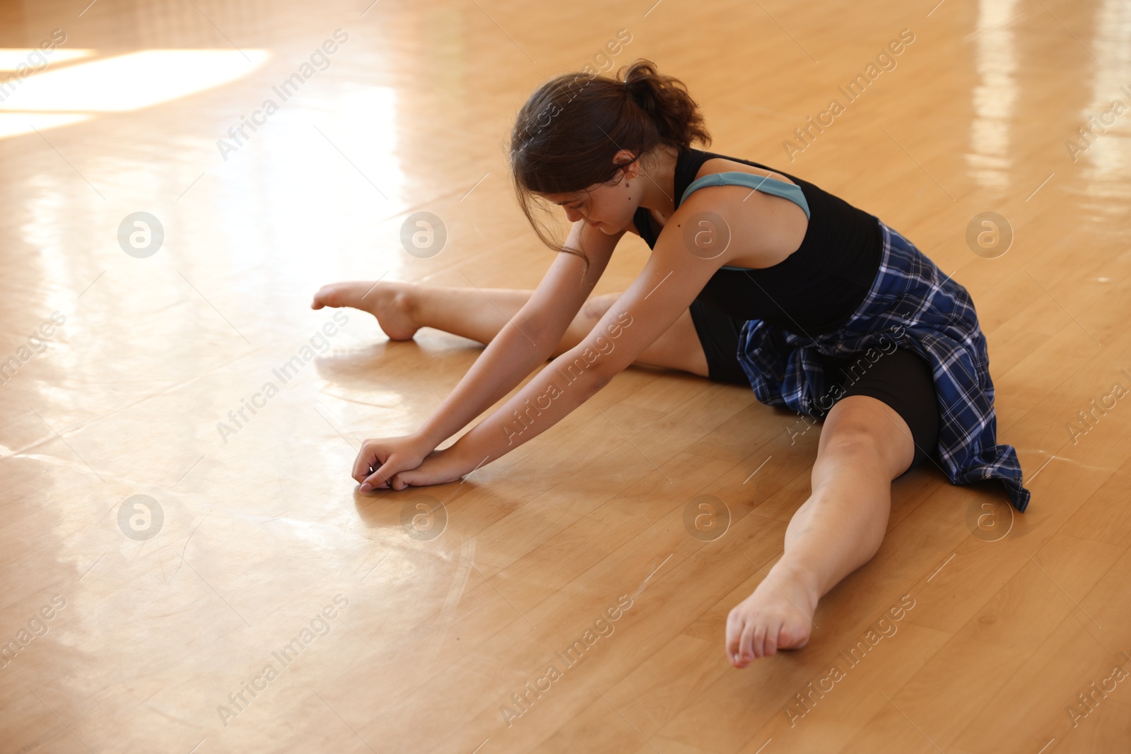 Teenage girl stretching on wooden floor indoors Photo of Teenage girl stretching on wooden floor indoors
