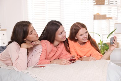 Photo of Happy friends taking selfie on bed at home