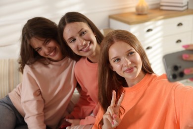 Photo of Happy friends taking selfie on bed at home