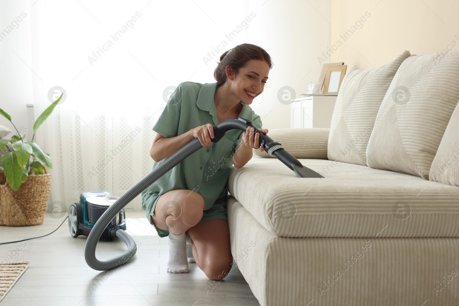 Woman cleaning sofa with vacuum cleaner at home Photo of Woman cleaning sofa with vacuum cleaner at home