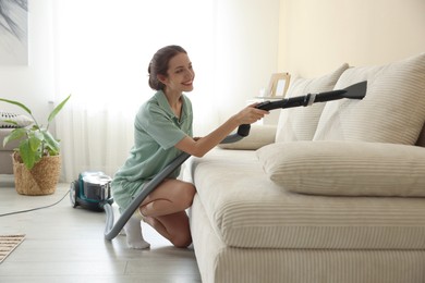 Photo of Woman cleaning sofa with vacuum cleaner at home