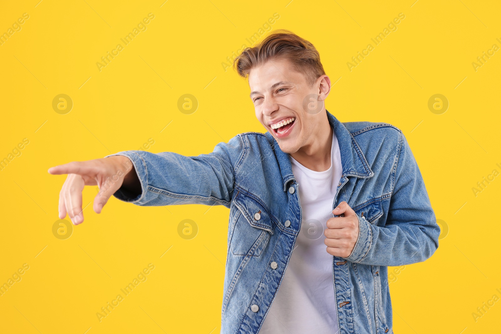 Handsome man laughing and pointing at something on yellow background. Positive emotion Photo of Handsome man laughing and pointing at something on yellow background. Positive emotion