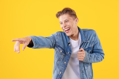 Photo of Handsome man laughing and pointing at something on yellow background. Positive emotion