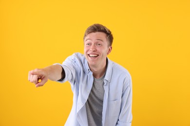 Photo of Handsome man laughing and pointing at something on yellow background. Positive emotion