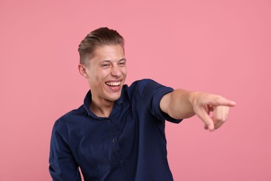 Photo of Handsome man laughing and pointing at something on pink background. Positive emotion