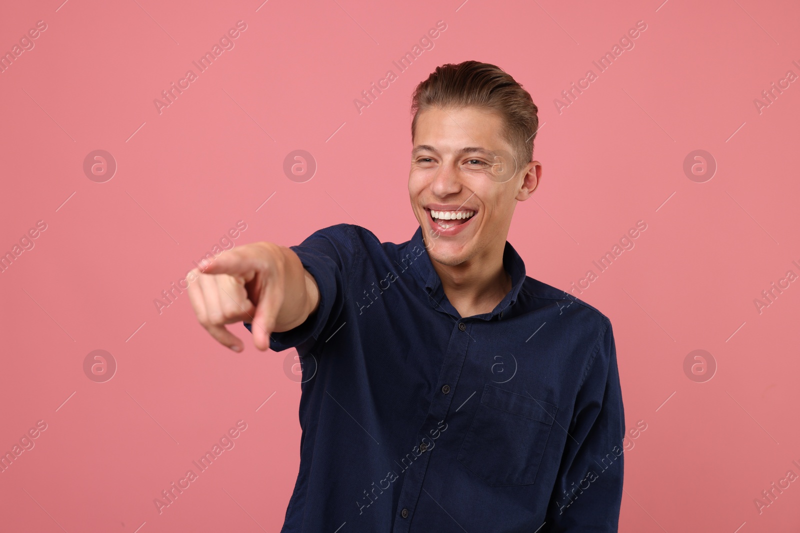 Handsome man laughing and pointing at something on pink background. Positive emotion Photo of Handsome man laughing and pointing at something on pink background. Positive emotion