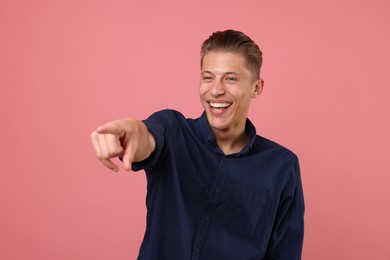 Photo of Handsome man laughing and pointing at something on pink background. Positive emotion