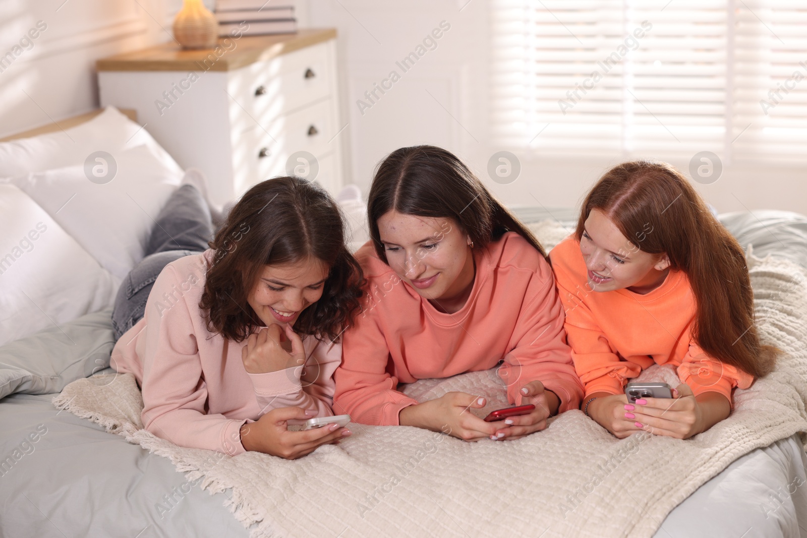 Friends with smartphones on bed at home Photo of Friends with smartphones on bed at home