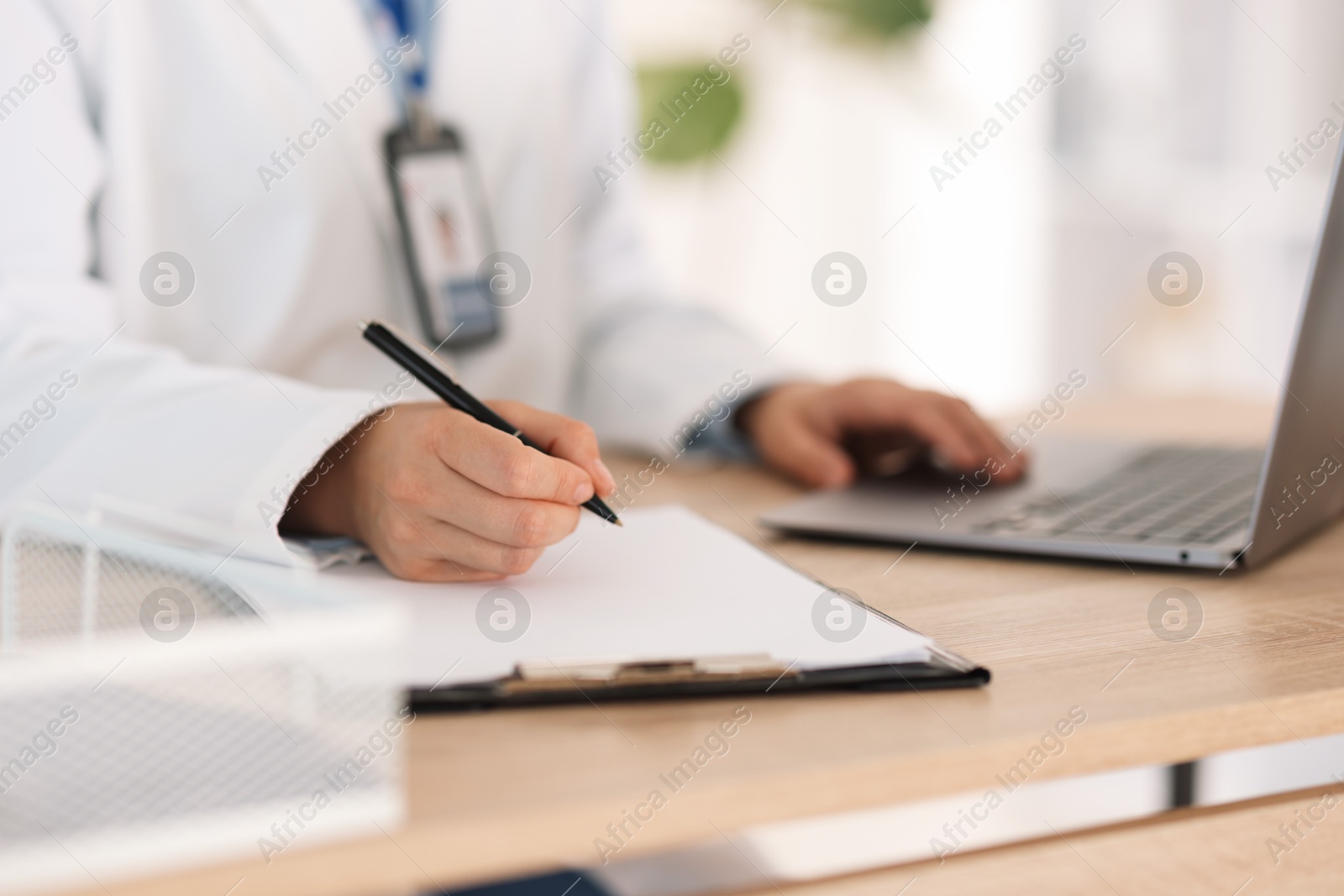 Photo of Telemedicine. Doctor making notes while having video call with patient via laptop indoors, closeup