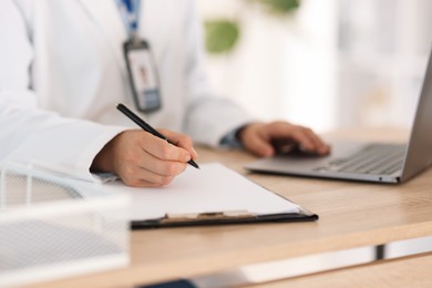 Photo of Telemedicine. Doctor making notes while having video call with patient via laptop indoors, closeup