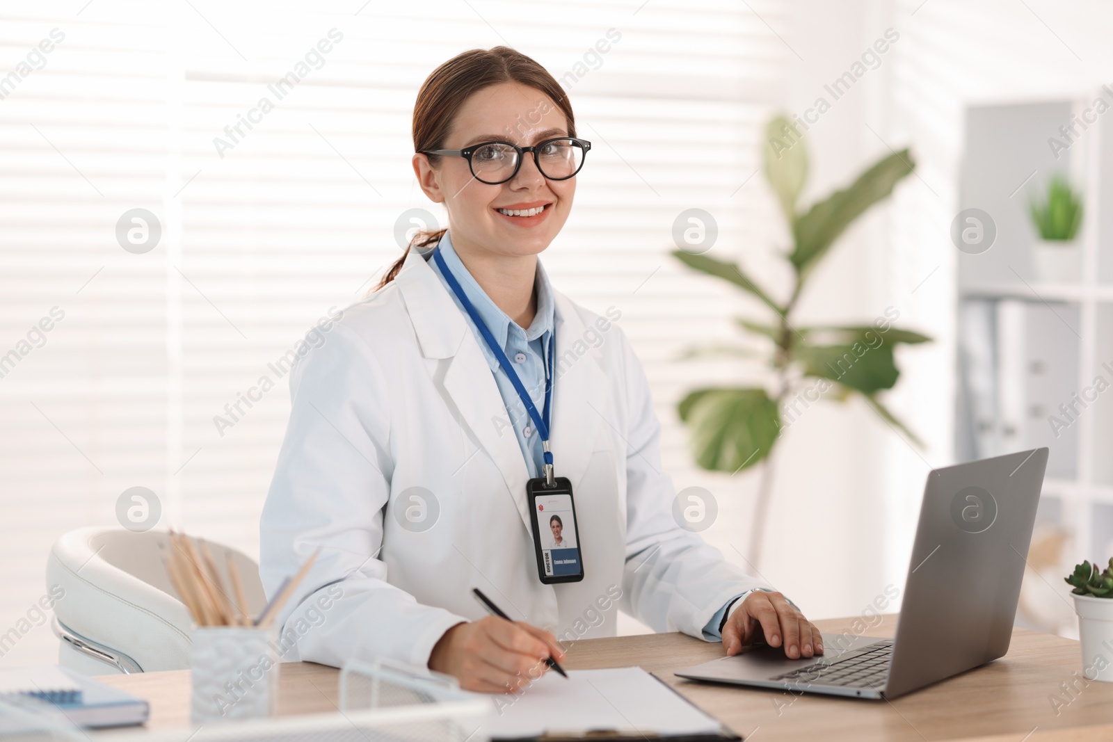 Photo of Telemedicine. Doctor making notes while having video call with patient via laptop indoors