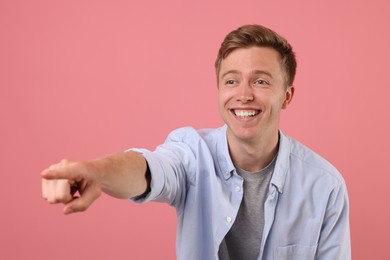 Photo of Handsome man laughing and pointing at something on pink background. Positive emotion