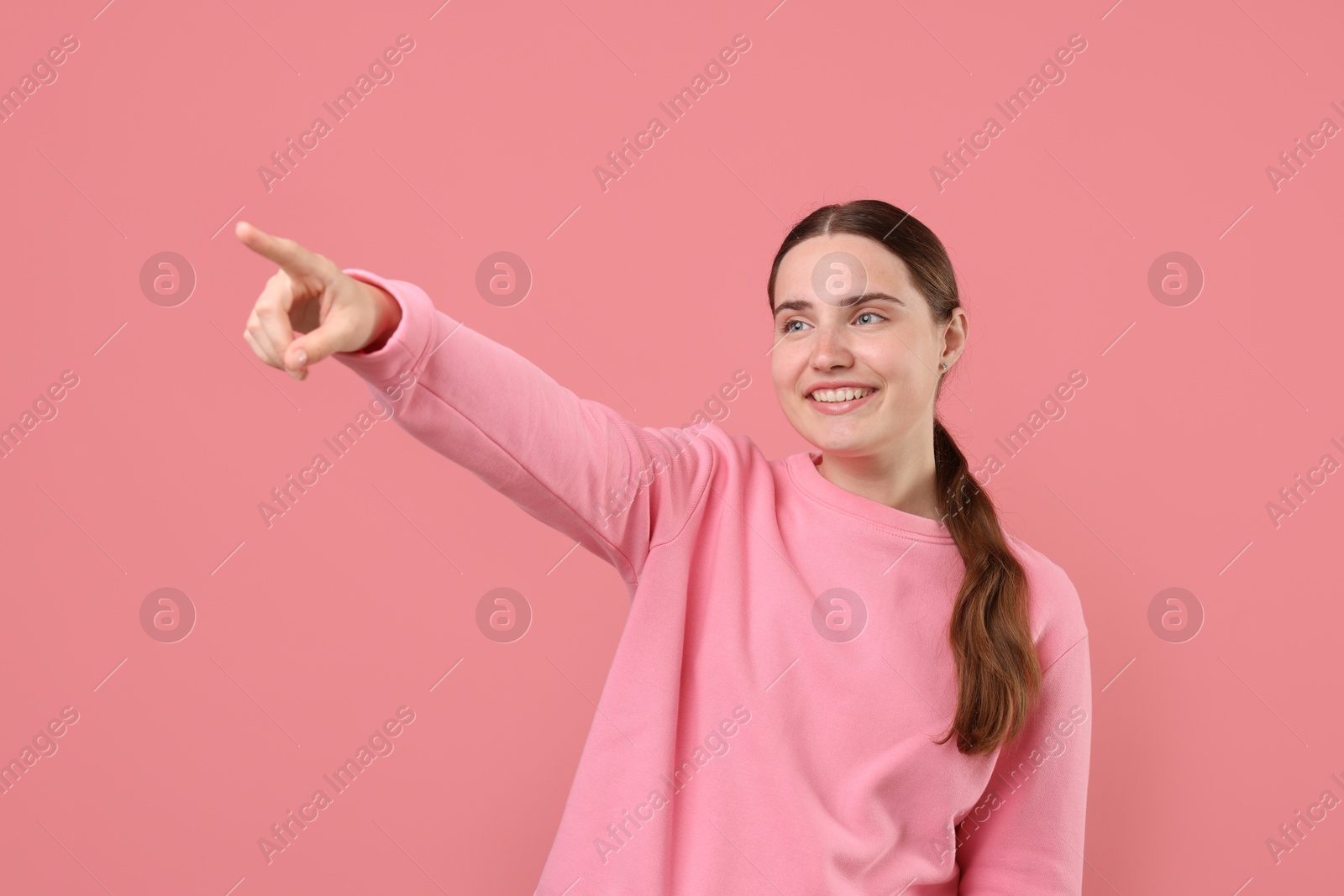 Beautiful woman laughing and pointing at something on pink background. Positive emotion Photo of Beautiful woman laughing and pointing at something on pink background. Positive emotion