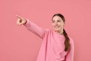 Photo of Beautiful woman laughing and pointing at something on pink background. Positive emotion