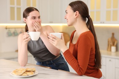 Photo of Women with coffee laughing in kitchen. Positive emotion