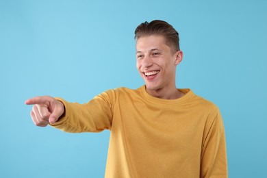 Photo of Handsome man laughing and pointing at something on light blue background. Positive emotion