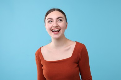 Photo of Beautiful woman laughing on light blue background. Positive emotion