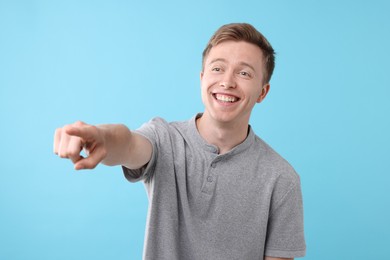 Photo of Handsome man laughing and pointing at something on light blue background. Positive emotion