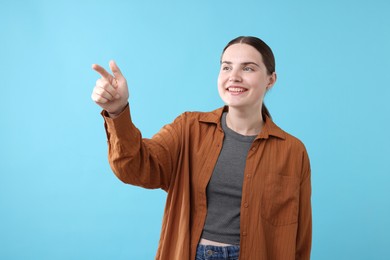 Photo of Beautiful woman laughing and pointing at something on light blue background. Positive emotion