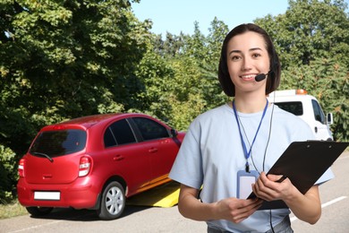 Image of Car service worker with headset and clipboard against vehicle and tow truck outdoors. Client support