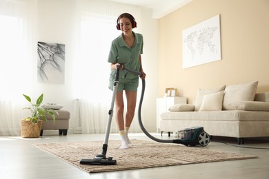 Photo of Woman in headphones cleaning carpet with vacuum cleaner at home, low angle view
