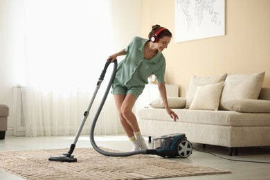 Photo of Woman in headphones cleaning carpet with vacuum cleaner at home