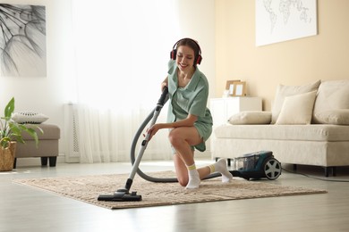 Photo of Woman in headphones cleaning carpet with vacuum cleaner at home