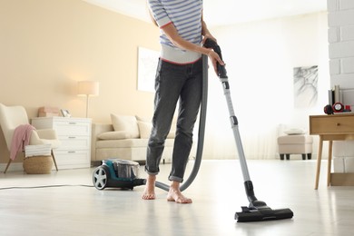 Photo of Woman cleaning floor with vacuum cleaner at home, closeup