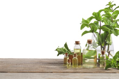 Photo of Bottles of essential oils, mint and thyme on wooden table against white background