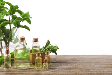 Photo of Bottles of essential oils, mint and thyme on wooden table against white background