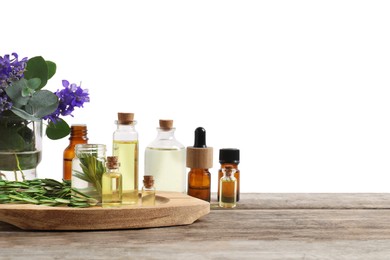 Photo of Bottles of essential oils and different plants on wooden table against white background