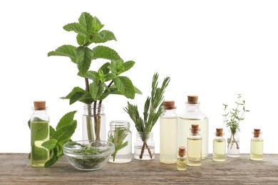 Photo of Bottles of essential oils and different herbs on wooden table against white background