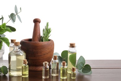 Photo of Bottles of essential oils and different plants on wooden table against white background