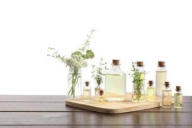 Photo of Bottles of essential oils and different herbs on wooden table against white background