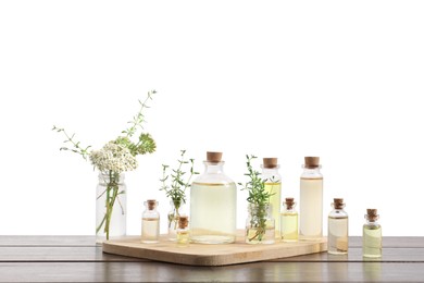 Photo of Bottles of essential oils and different herbs on wooden table against white background