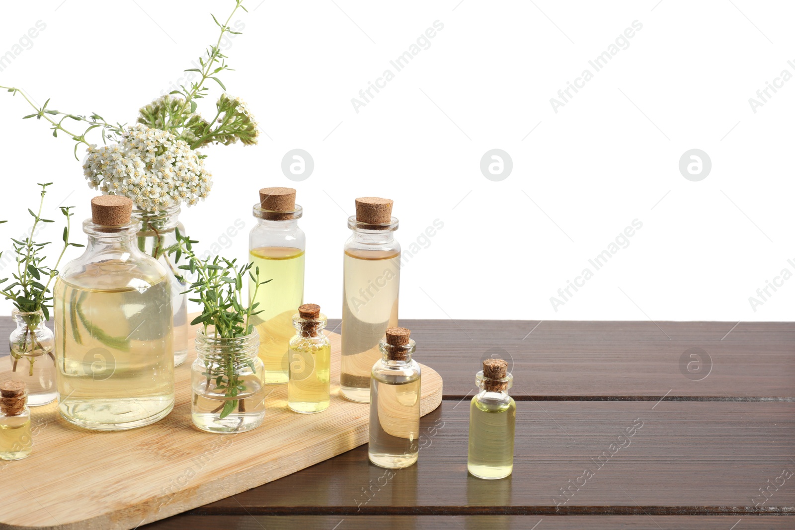 Bottles of essential oils and different herbs on wooden table against white background Photo of Bottles of essential oils and different herbs on wooden table against white background