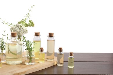 Photo of Bottles of essential oils and different herbs on wooden table against white background
