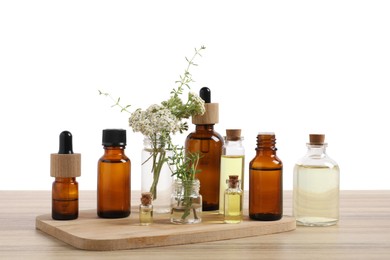 Photo of Bottles of essential oils and different herbs on wooden table against white background