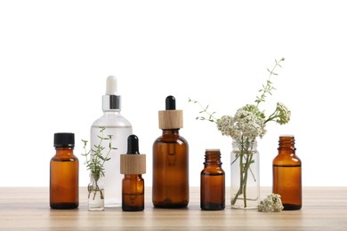 Photo of Bottles of essential oils and different herbs on wooden table against white background