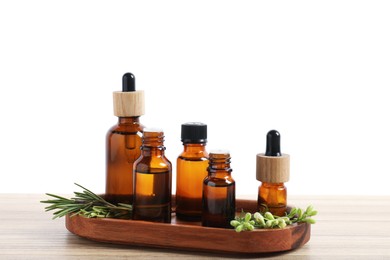 Photo of Bottles of essential oils and different herbs on wooden table against white background