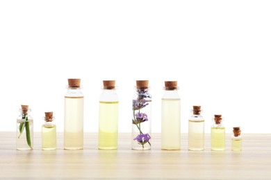 Photo of Bottles of essential oils with herbs on wooden table against white background