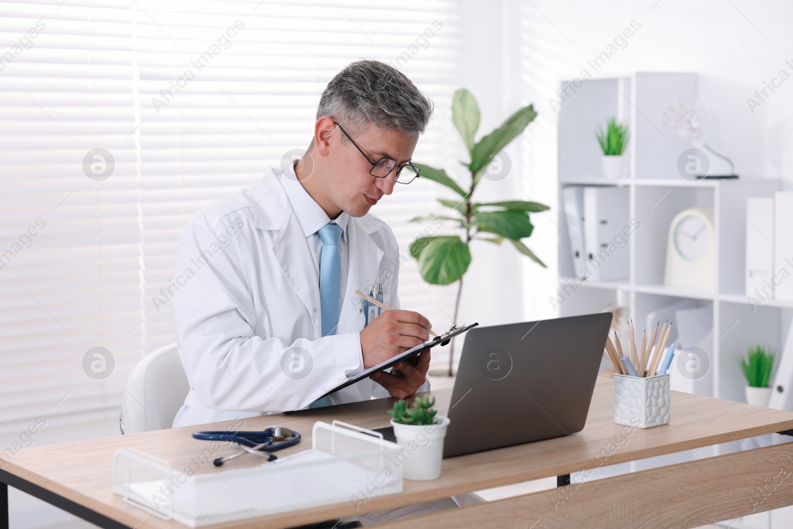 Photo of Telemedicine. Doctor making notes while having video call with patient via laptop indoors