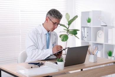 Photo of Telemedicine. Doctor making notes while having video call with patient via laptop indoors