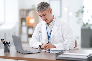 Photo of Telemedicine. Doctor making notes while having video call with patient via laptop indoors