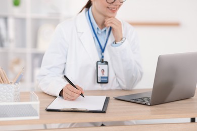 Photo of Telemedicine. Doctor making notes while having video call with patient via laptop indoors, closeup