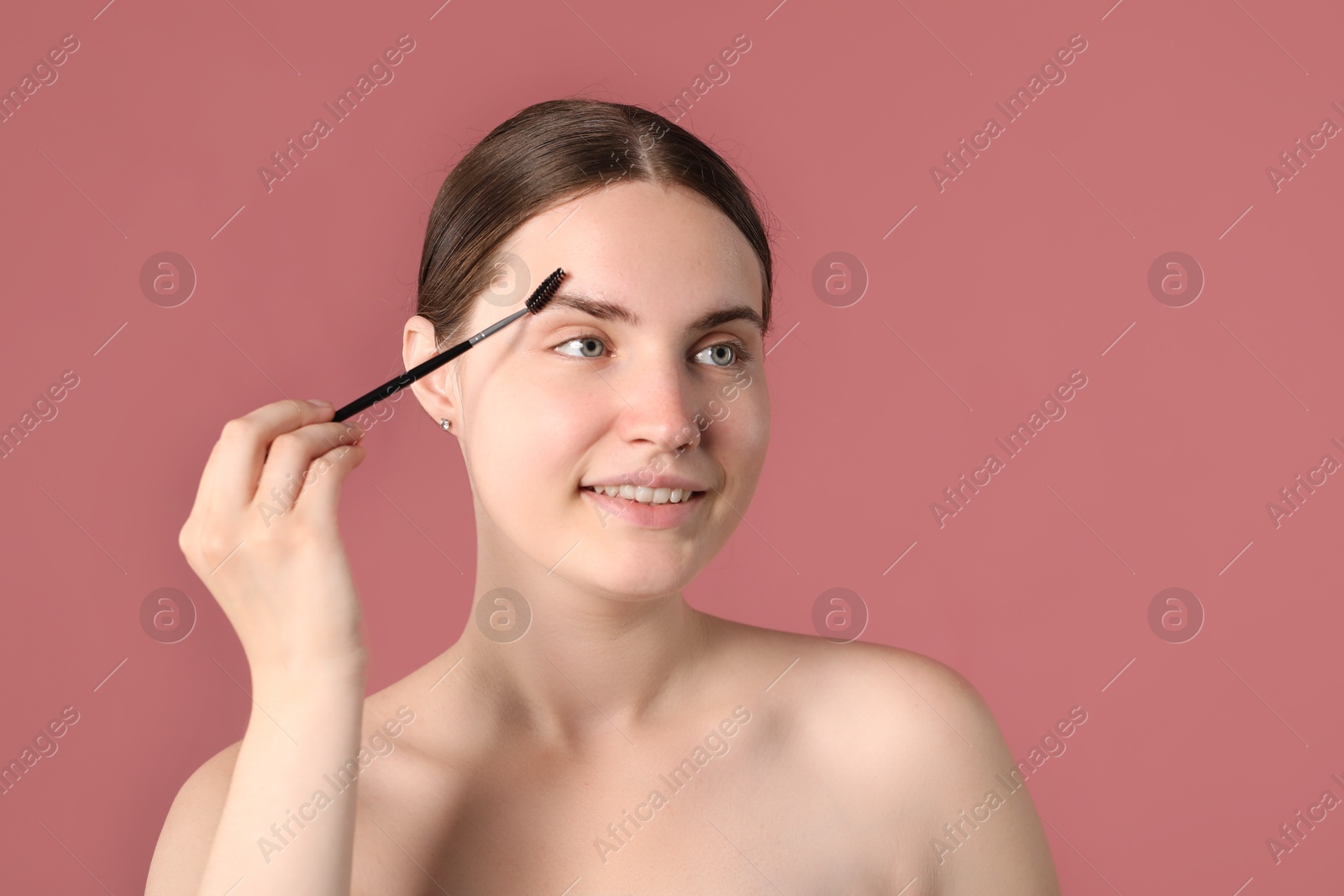 Photo of Young woman brushing her eyebrow with spoolie on pink background