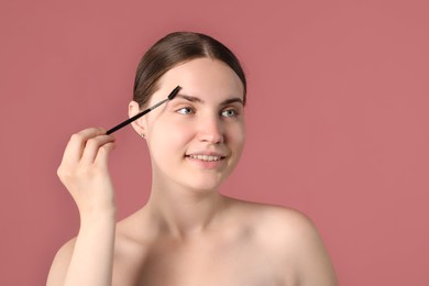Photo of Young woman brushing her eyebrow with spoolie on pink background