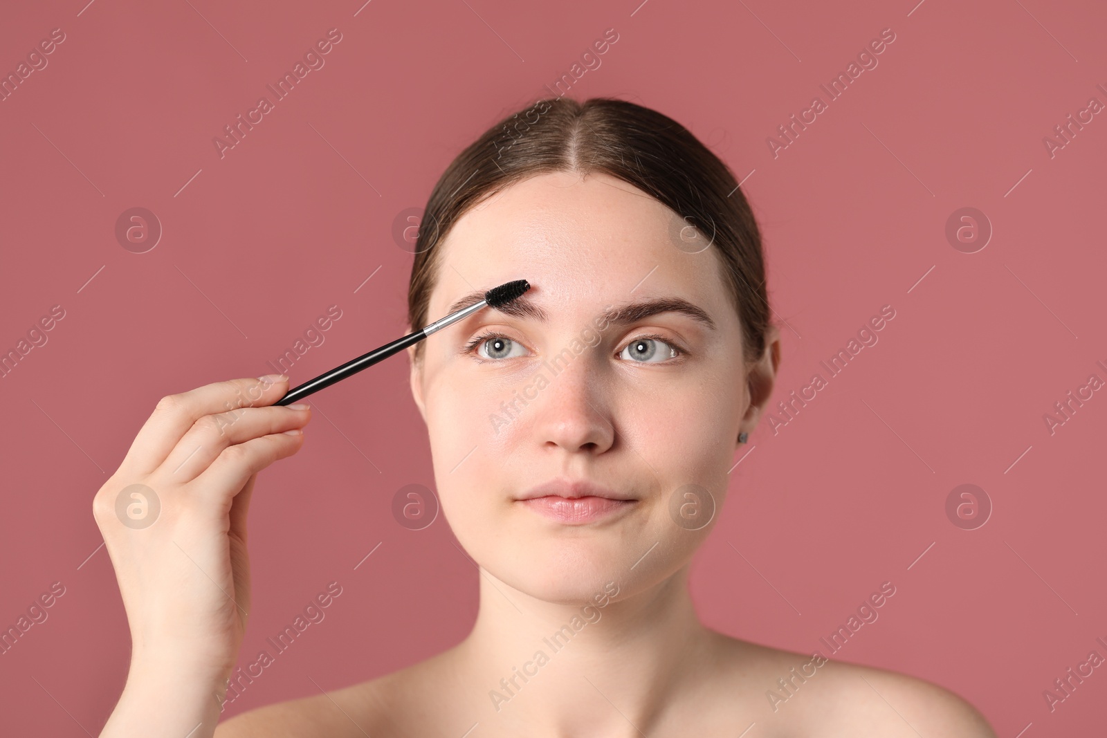 Photo of Young woman brushing her eyebrow with spoolie on pink background